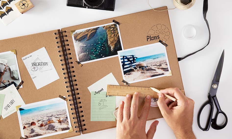 This is a travel scrapbook with the corners of photos and postcards stuck on with washi tape. There is a ruler and a pencil on the page.