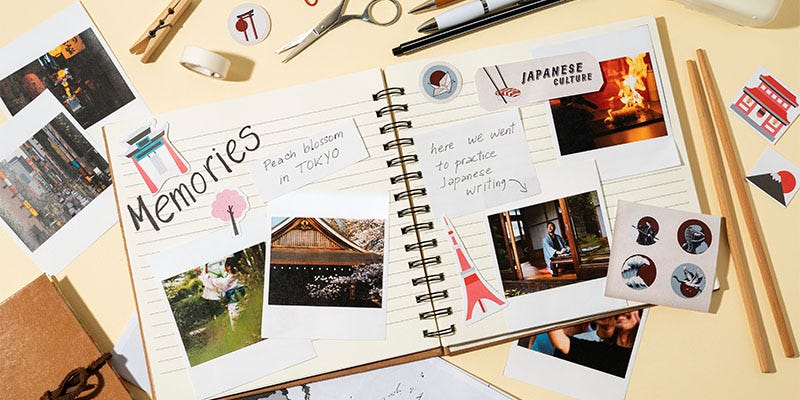 This is a travel-themed open scrapbook page. It features letter stickers saying memories, some Japanese-style stickers and photos. The desk is full of stationery, washi tape and chopsticks.