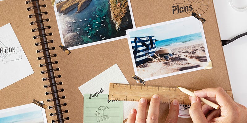 This is a travel scrapbook with the corners of photos and postcards stuck on with washi tape. There is a ruler and a pencil on the page.