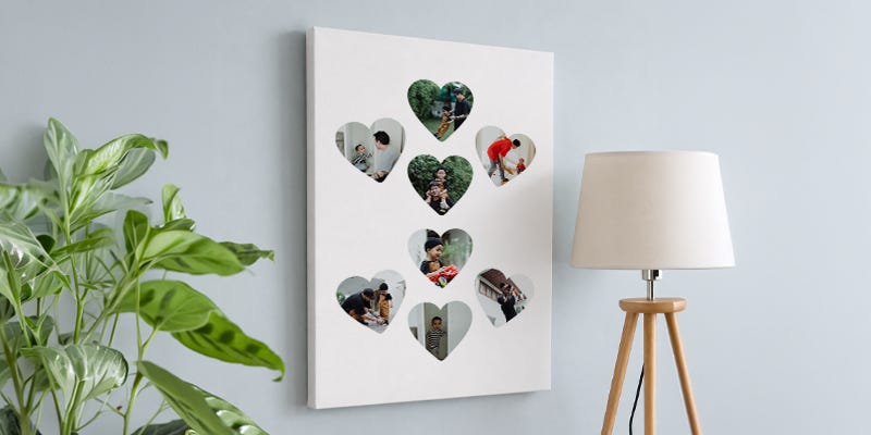 A love heart collage displayed on a wall between a lamp and a plant.