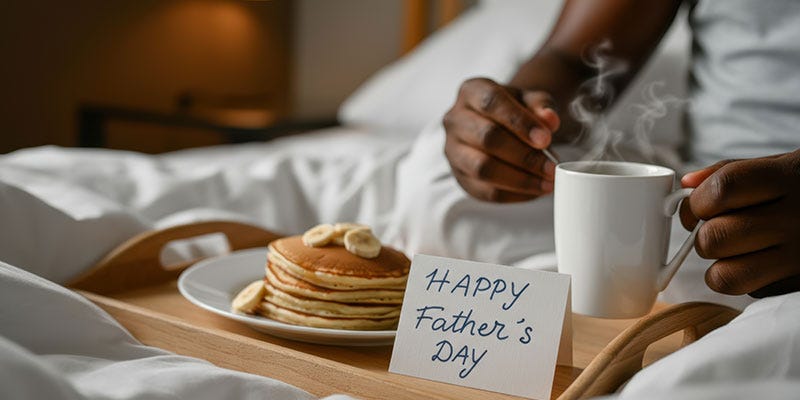 Father's Day breakfast in bed. There is a tray with a stack of pancakes and a card saying 'Happy Father's Day'.